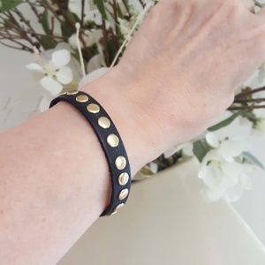 A person wearing a black leather bracelet with gold studs.