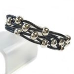 A black leather bracelet with silver beads on it.