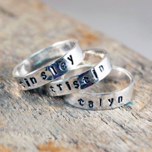 Three silver rings with names on them sitting on top of a table.